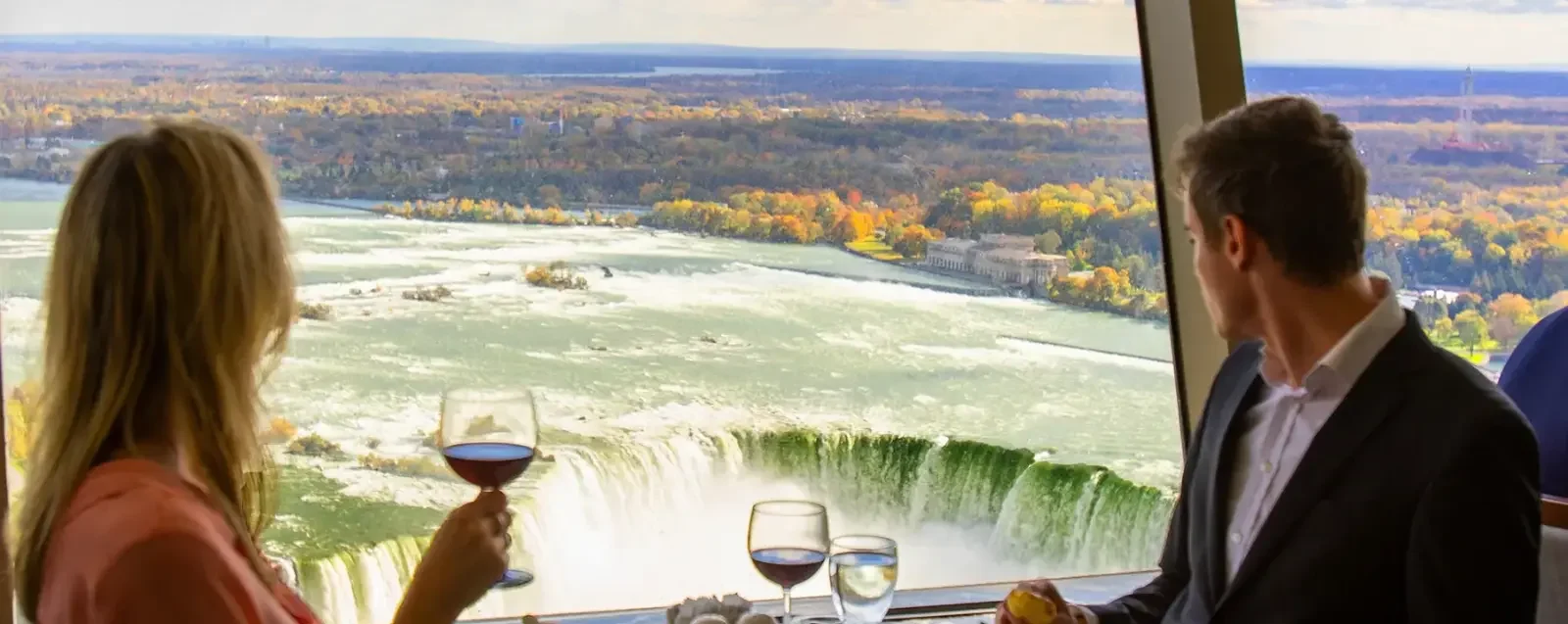 A couple dining at a window table above the falls with autumn colour beyond